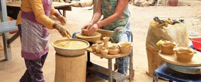 A Cambodian woman teaches a senior volunteer traditional Khmer pottery. An older volunteer participates in a pottery class as part of her Khmer cultural experience in Cambodia.